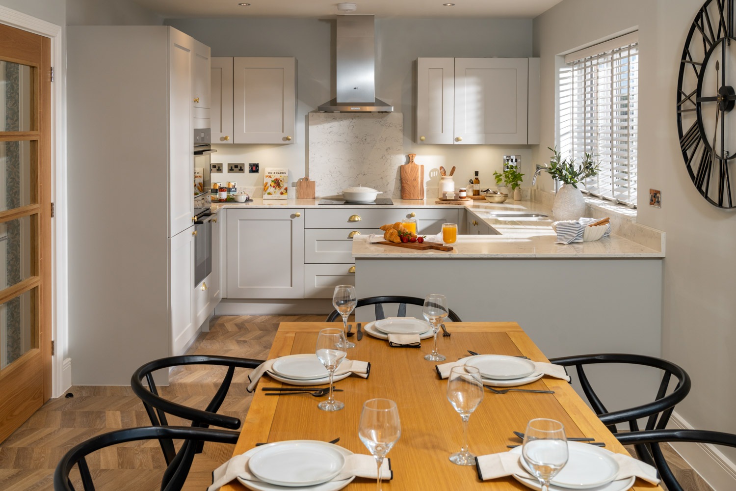dining table and chairs a forefront of image. grey kitchen to the rear with wooden flooring and marble worktops