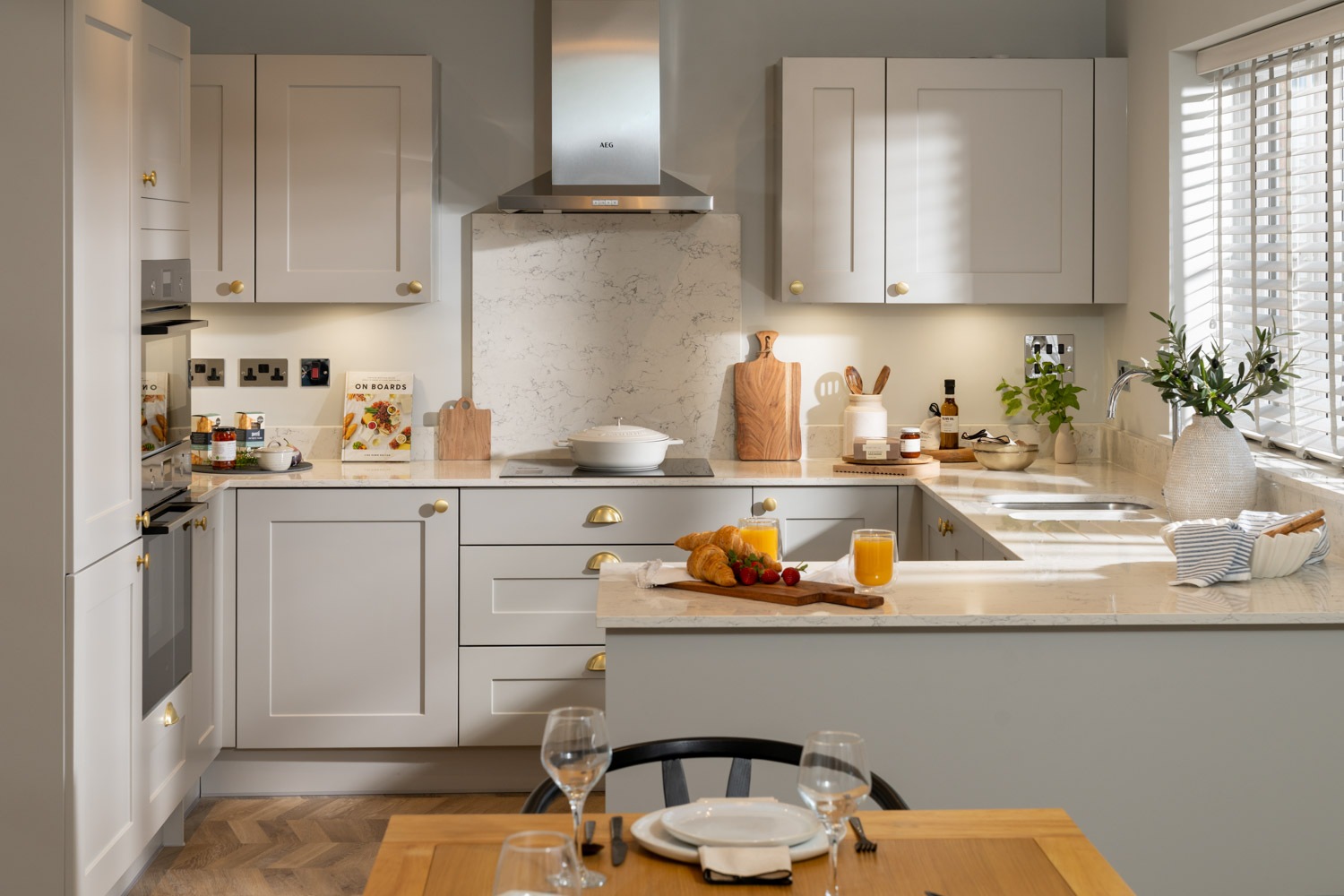 dining table and chairs a forefront of image. grey kitchen to the rear with wooden flooring and marble worktops